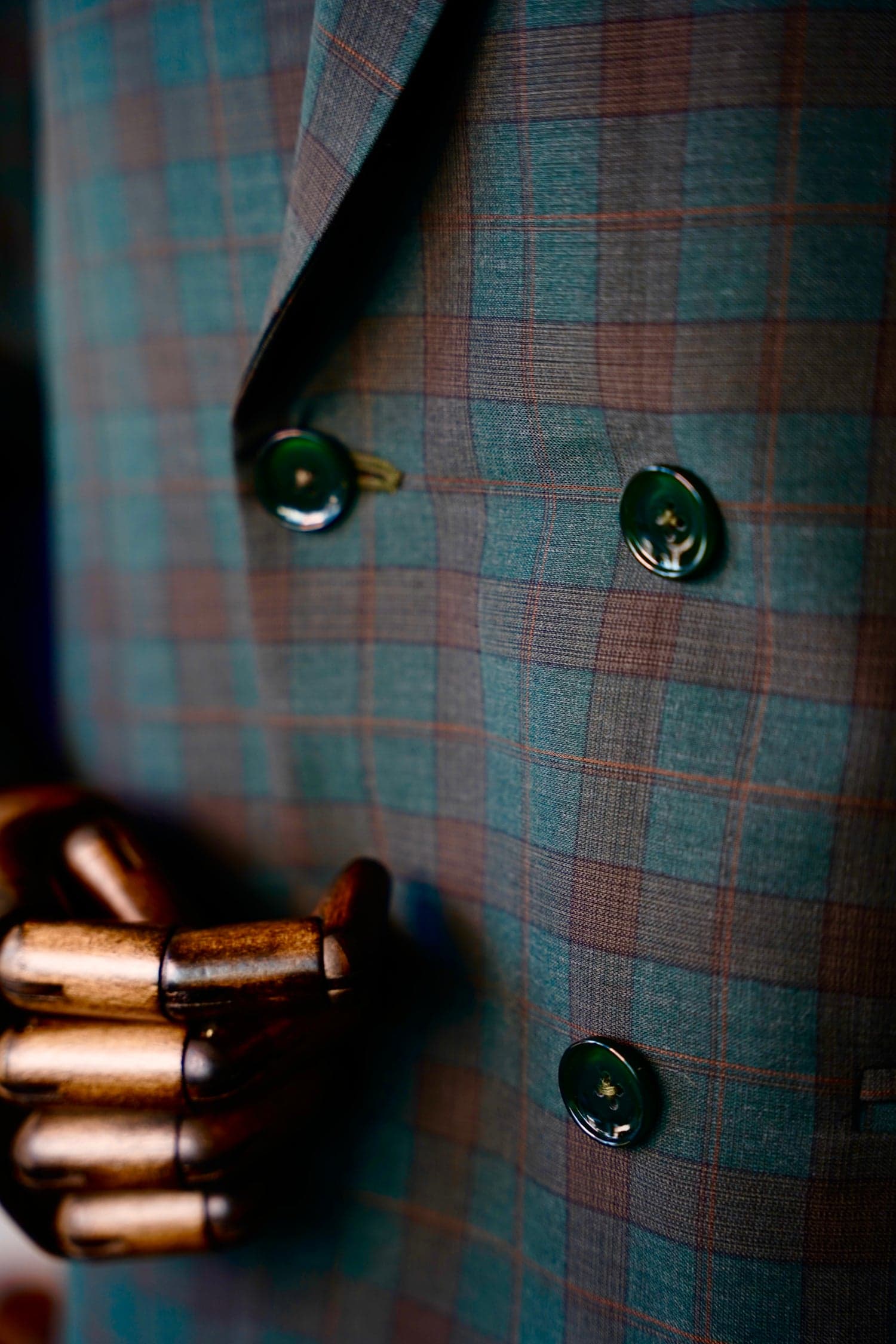 Macro of teal and rust plaid double-breasted buttons on a wooden mannequin hand