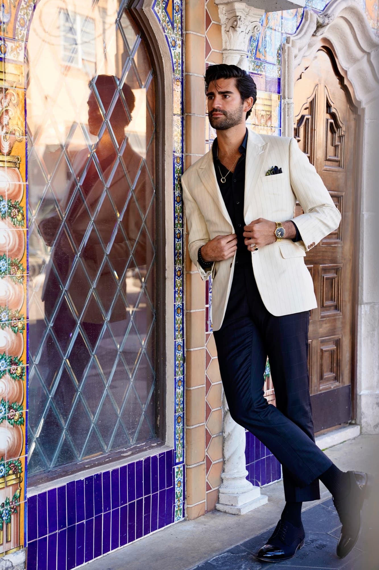 Cream jacket with black shirt by a leaded-glass window